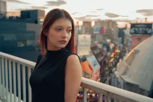 A female model posing on the balcony against the Shibuya cityscape. The emotional light of dusk.