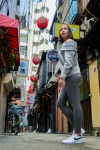 Portrait of a woman looking back over her shoulder in a narrow Shibuya yokocho alley strung with red lanterns, by JG.